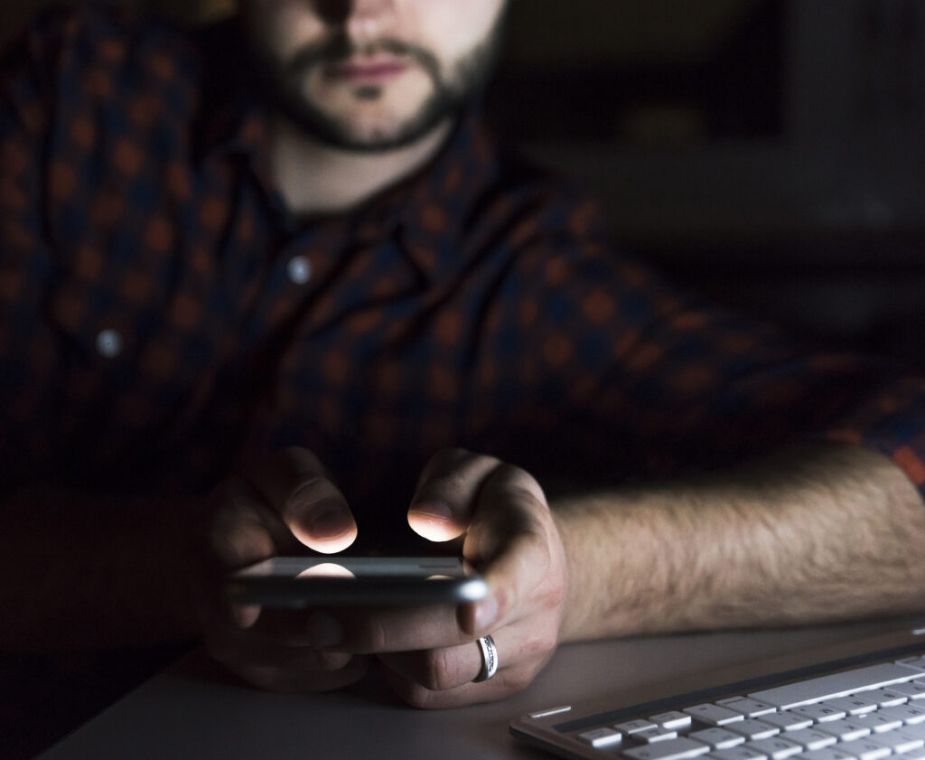 Man lit only by his phone screen, scrolling late at night in a dark room