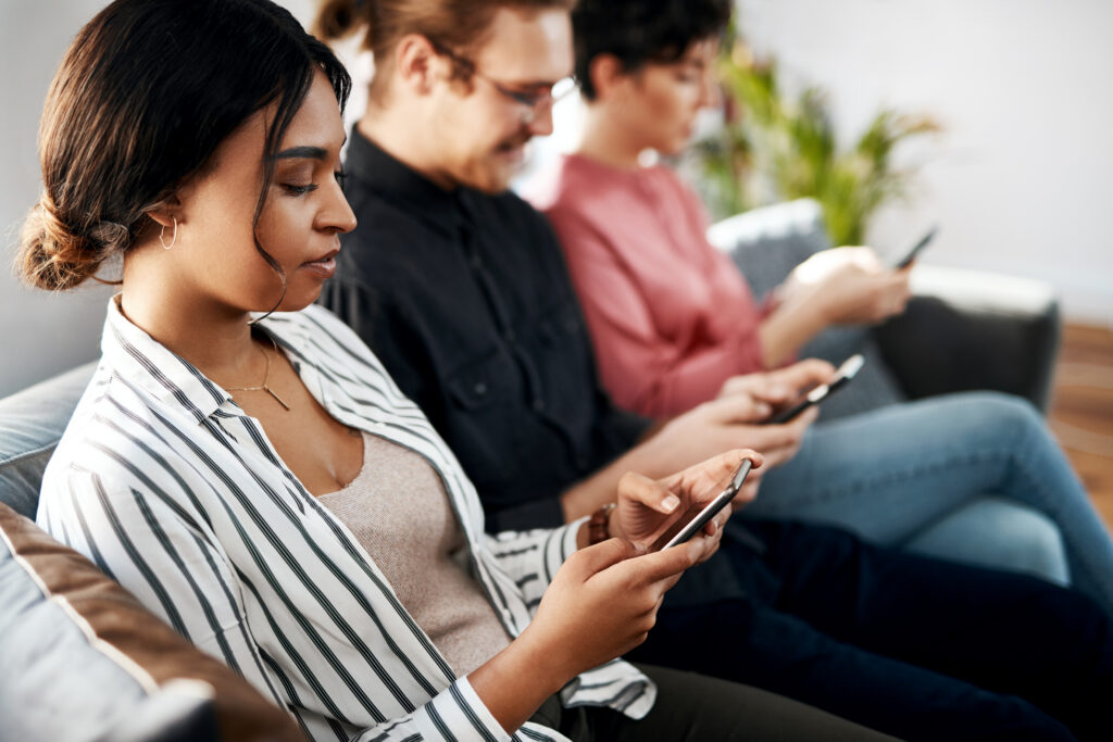 Three friends side by side on a couch, each absorbed in their own phone